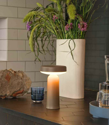 Tragbare Muuto Tischleuchte auf dunkler Küchenarbeitsplatte mit floraler Dekoration.