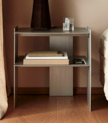 Schmaler Nachttisch aus Metall mit zwei Ablagen, Büchern, Glas und Vase neben einem Bett.
