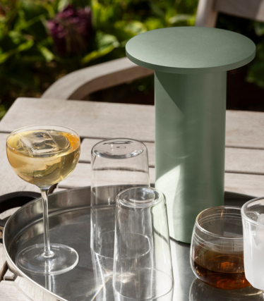Salbeigrüner, zylindrischer Beistelltisch/Kühler auf einem Tablett mit Gläsern und Getränken im Freien.
