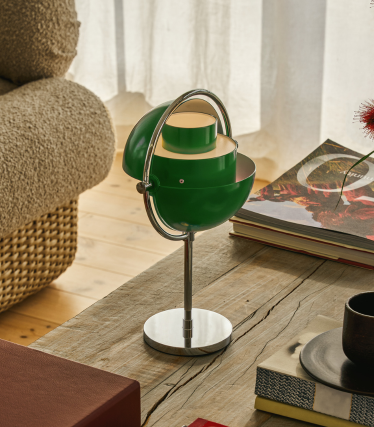 Grüne Multi-Lite Tischleuchte mit Chromfuß auf einem Holztisch neben Büchern.